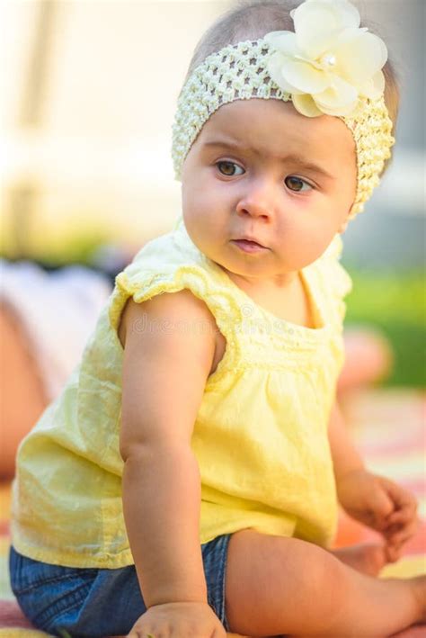 Portrait Of Cute Baby Girl In Yellow Band And Dress Sits In Sunny