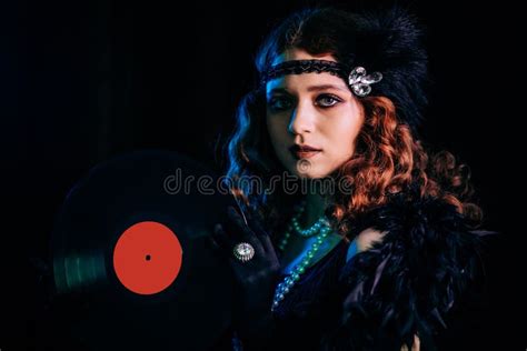 old fashioned woman dressed in style of flappers posing with vinyl record on dark background