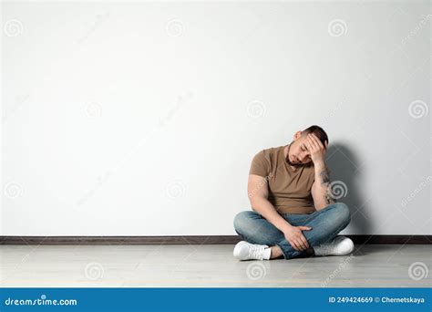 Sad Young Man Sitting On Floor Near White Wall Indoors Space For Text