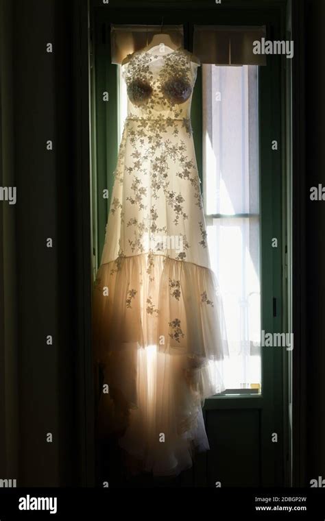 Backlit Elegant Wedding Dress Hanging In A Window Showing The Delicate