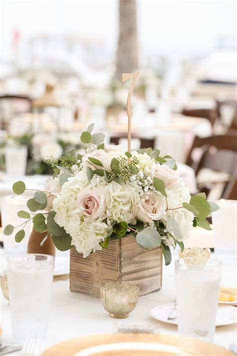 A Centerpiece With White Flowers And Greenery Sits On A Table At A