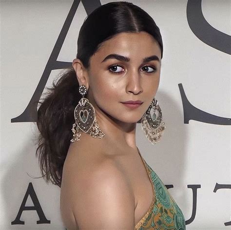 A Woman In A Green And Gold Dress Posing For The Camera With Large Earrings On Her Neck