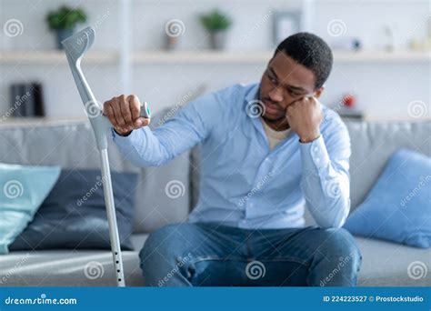 Unhappy African American Guy Leaning On Crutch Suffering From