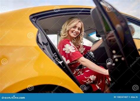 Photo Of Happy Blonde In Red Dress Sitting In Back Seat Of Yellow Taxi With Open Door Stock