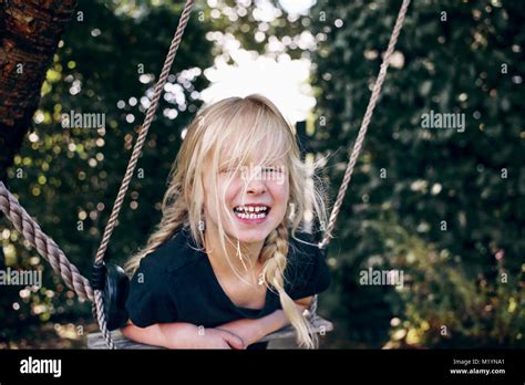 laughing little blonde girl happily playing alone on a tree swing in her backyard on a sunny day