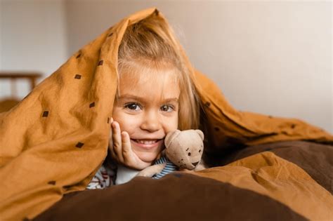 Милая маленькая девочка уютно лежит в постели покрытая одеялом на