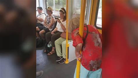 photo of elderly woman standing on train ignored by headphone wearing seated passengers divides