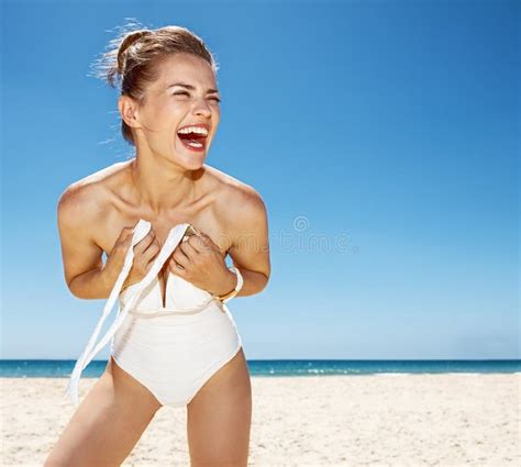 Smiling Woman Tying White Swimsuit At Sandy Beach On Sunny Day Stock