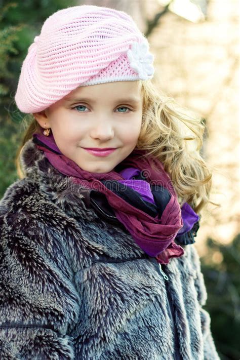 Маленькая девочка с голубыми глазами в розовой шляпе сидя в лесе