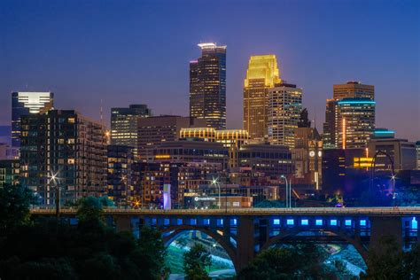 The City Skyline Is Lit Up At Night With Lights On And Bridge In