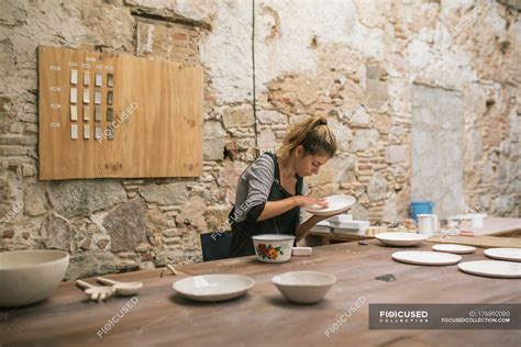 Concentrated Woman In Apron Sitting At Table And Forming Plates From