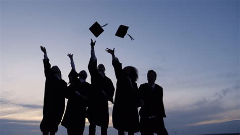 Silhouette Of Graduating Students Throwing Caps In The Air Stock Photo