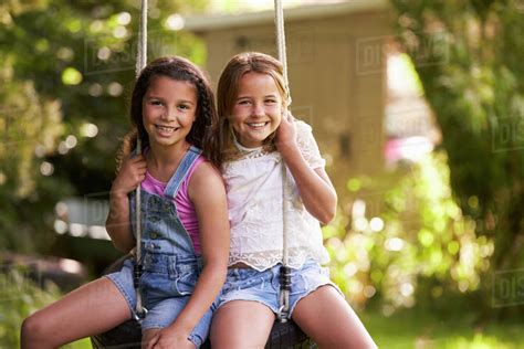 Portrait Of Two Girls Playing On Tire Swing In Garden Stock Photo