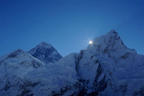 The Sun Shines Brightly Above Some Snow Covered Mountain Peaks In The