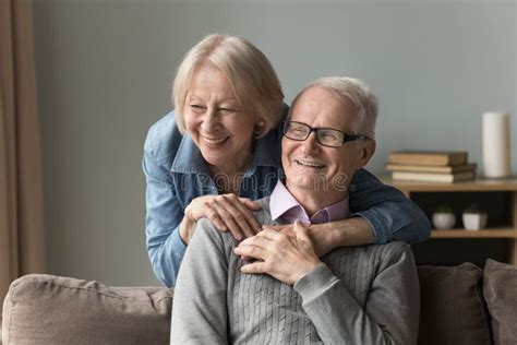 Senior Wife Hugs His Husband Resting On Sofa At Home Stock Image