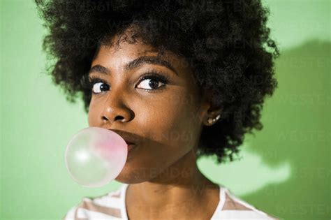 Young Woman Blowing Bubble Gum While Standing Against Green Background