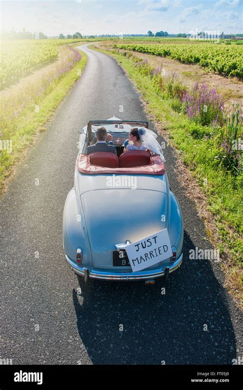 A Newlywed Couple Is Driving A Retro Car On A Country Road For Their