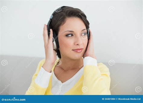 fundersam tillfällig brunett i den gula koftan som lyssnar till musik med hörlurar arkivfoto
