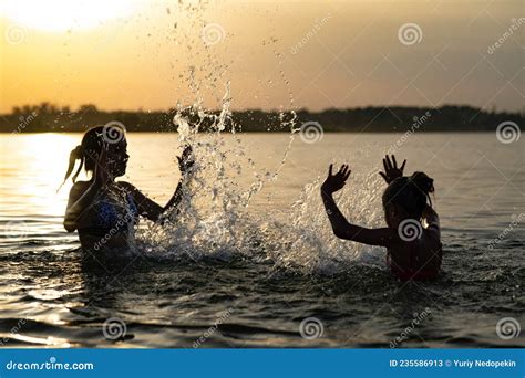 Two Sisters Splashing Water Playing In The Lake At Sunset Background