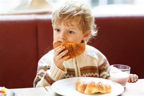 Cute Healthy Kid Boy Eating Croissant And Drinking Strawberry Milkshake