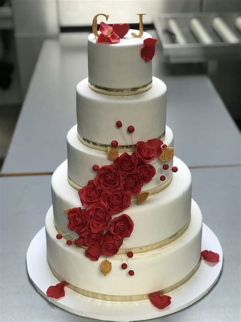 a three tiered wedding cake with red roses on the bottom and gold trimmings