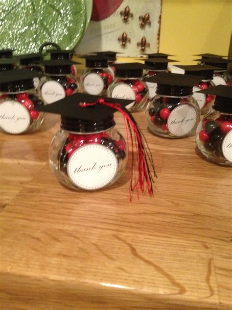 Many Small Glass Jars With Black Caps And Red Tassels Are On A Wooden Table