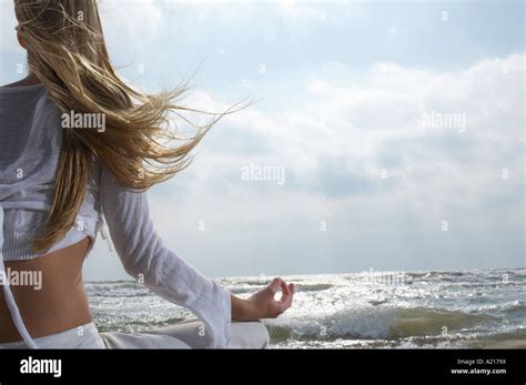 Young Woman Meditating On Beach Facing Ocean Back View Stock Photo