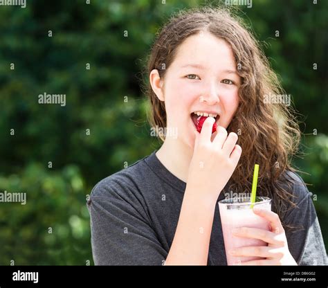 Photo Of Young Girl Eating Whole Strawberry While Holding Milkshake In Other Hand With Blurred