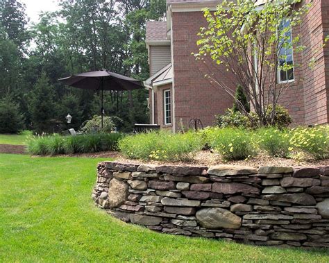 A Stone Wall In Front Of A Brick House With An Umbrella Over The Grass Area
