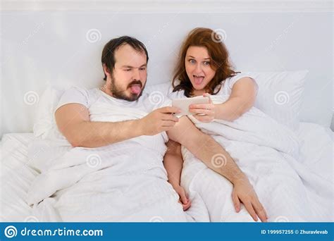A Man And A Woman Take A Selfie Photo Funny In A White Bed Husband And
