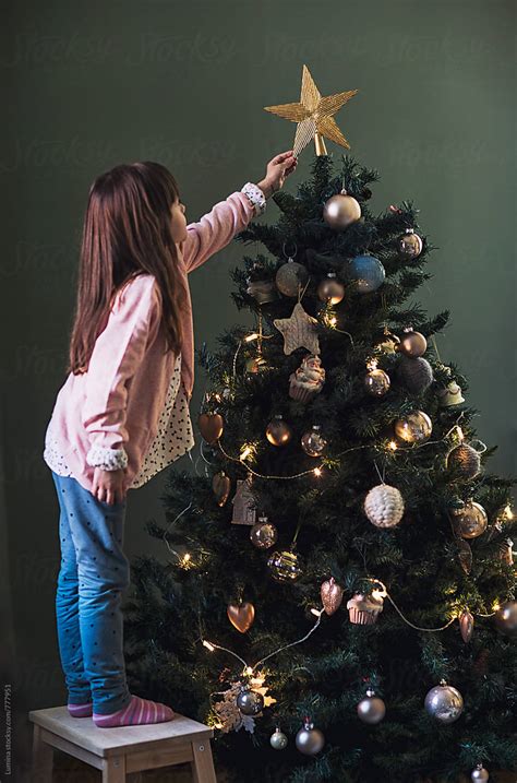 Girl Puts A Star On Top Of The Christmas Tree By Stocksy Contributor