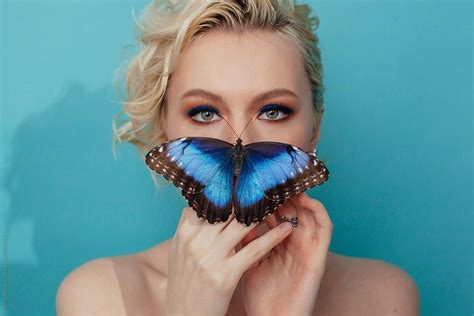 amazing blond woman holding big blue butterfly in front of her lips by liliya rodnikova blue