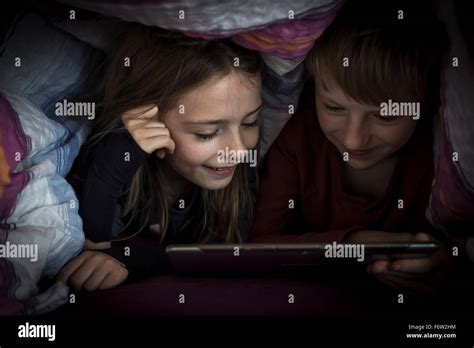 Brother And Sister Lying Side By Side Using Digital Tablet Under A