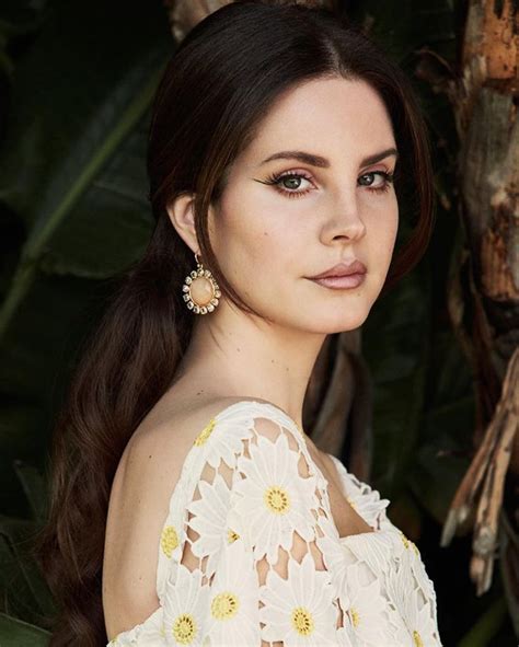 a woman with long brown hair wearing large earrings and a white dress is looking at the camera