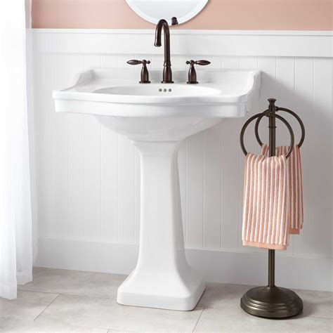 A white pedestal sink fitted with a chrome hook and spout faucet is mounted against white hexagon floor tiles in front of white subway backsplash tiles lining an upper wall covered in cole & son frontier wallpaper. Cierra Large Porcelain Pedestal Sink - Pedestal Sinks ...