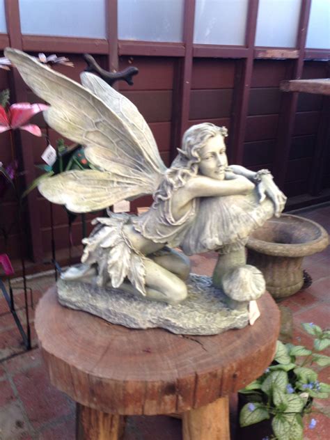 A Statue Of A Fairy Sitting On Top Of A Wooden Table Next To A Potted Plant