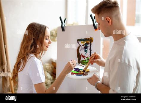 Young Amazing Fair Haired Couple In White T Shirts Stand Near Canvas