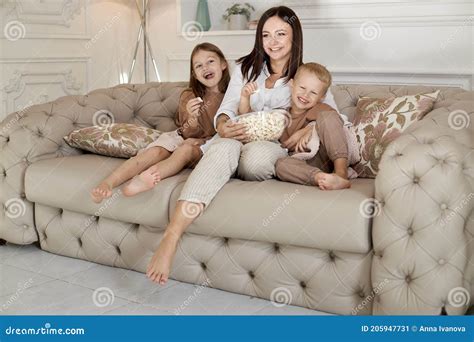 Mom Sits On The Couch With Her Son And Daughter And Watch A Movie A