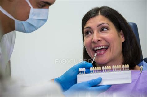 Dentist Examining Female Patient With Teeth Shades At Dental Clinic