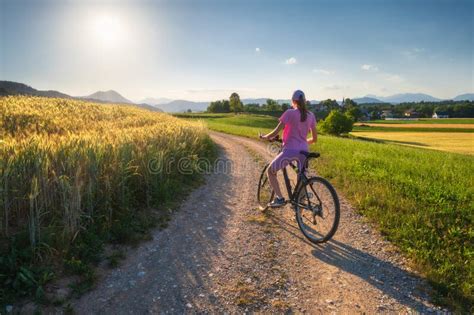 Woman On Mountain Bike On Gravel Road At Sunset In Summer Stock Photo