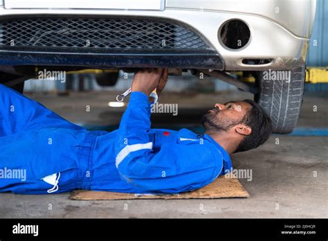 Profgessional Car Mechanic Lying Down While Working Under Car At Garage