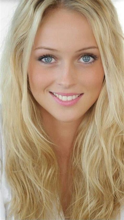 a woman with long blonde hair and blue eyes smiles at the camera while wearing a white shirt