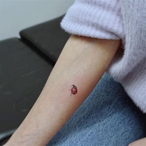 a ladybug tattoo on the left arm and right arm is shown in red ink