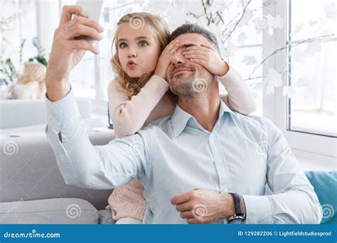 Hija Que Cubre Ojos Del Padre Y Que Hace Muecas Mientras Que Ellos Foto