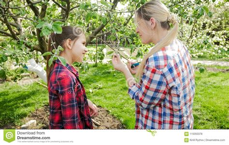 Young Smiling Woman Showing Her Daughter How To Take Care Of Trees In
