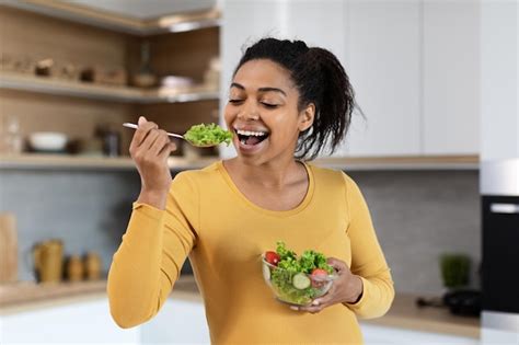Портрет веселой молодой чернокожей беременной женщины с большим животом поедающей салат с