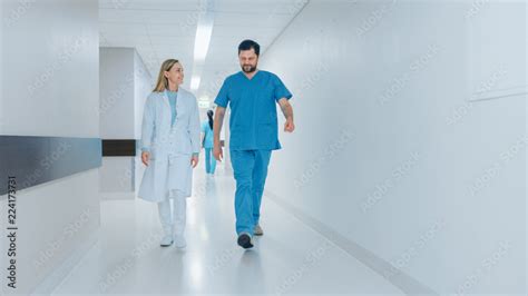 Surgeon And Female Doctor Walk Through Hospital Hallway In A Hurry