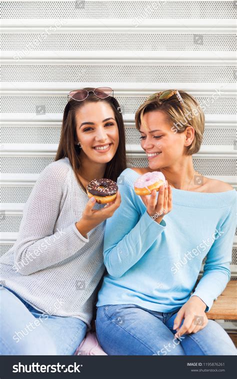 Two Beautiful Young Women Eating Donuts Stock Photo 1195876261