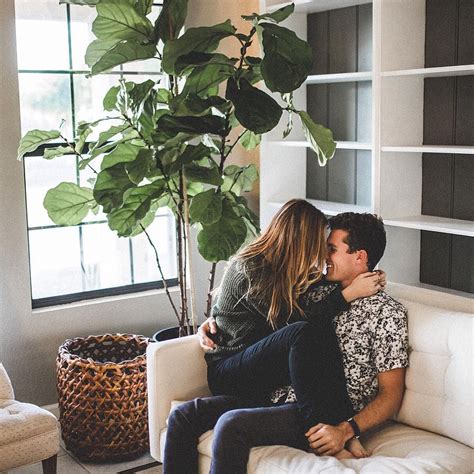 A Man And Woman Sitting On A White Couch In Front Of A Potted Plant