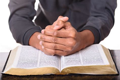 Hands Of A Young Man Folded Praying Over A Bible Hands Over Soft Focus
